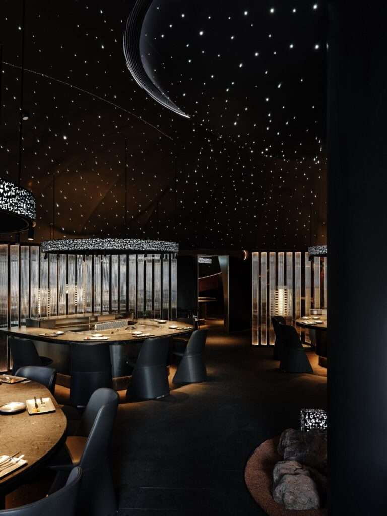 Modern Teppanyaki restaurant dining area featuring circular black marble cooking stations, dark leather chairs, textured glass partitions, and an immersive starry sky ceiling installation.