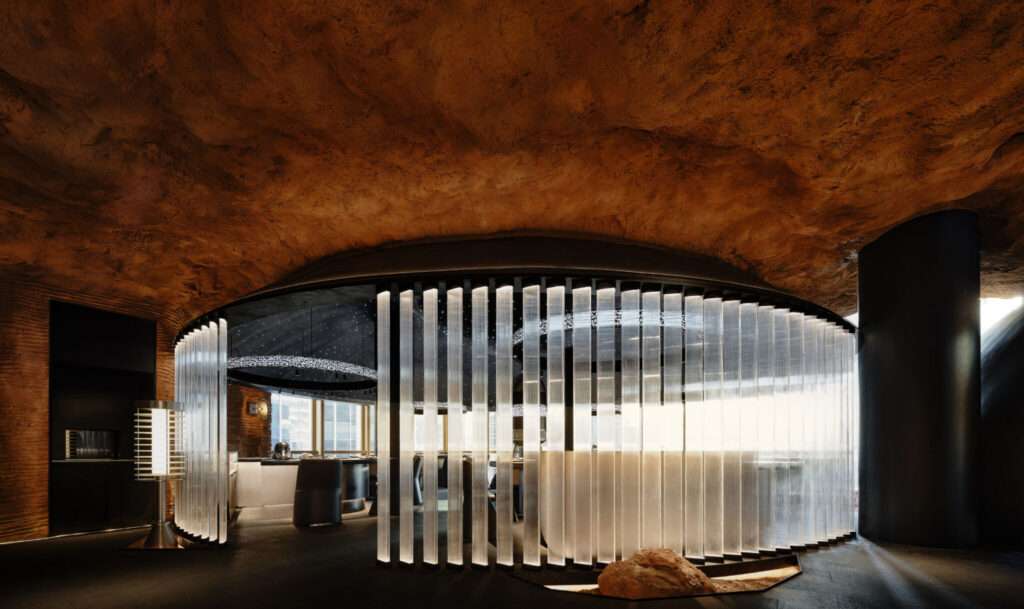 Panoramic view of a restaurant interior featuring massive, curved black matte sculptural pods resting on red earth beneath an organic, earth-toned rock ceiling.