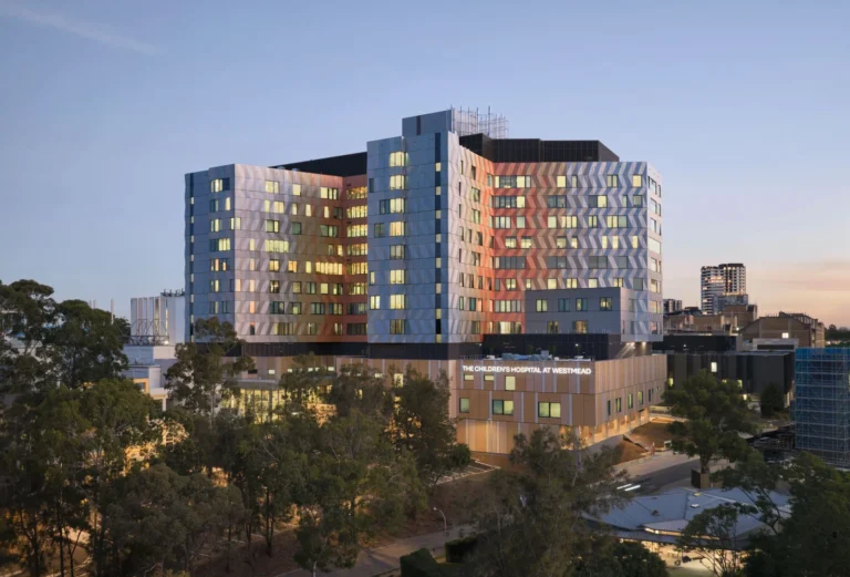 Exterior view of a multi-story medical building with a patterned multi-colored facade behind a tree line.