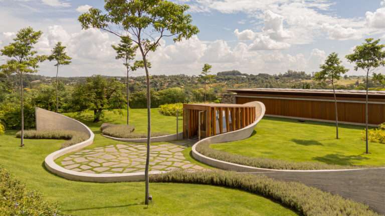 An aerial view of Nest Chapel in São Paulo featuring winding concrete walls and a central timber volume on a green lawn.