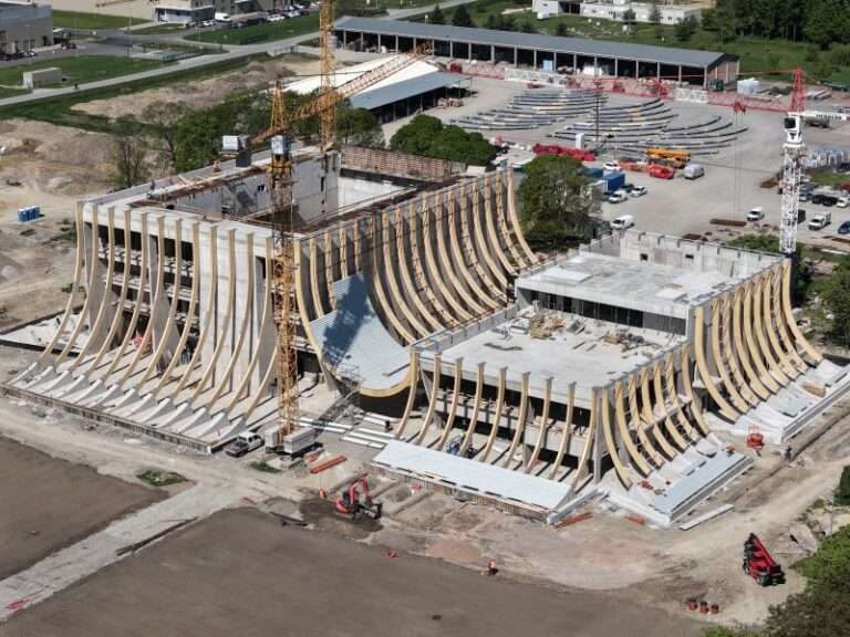 An aerial view of a concrete building under construction with curved timber framing systems.