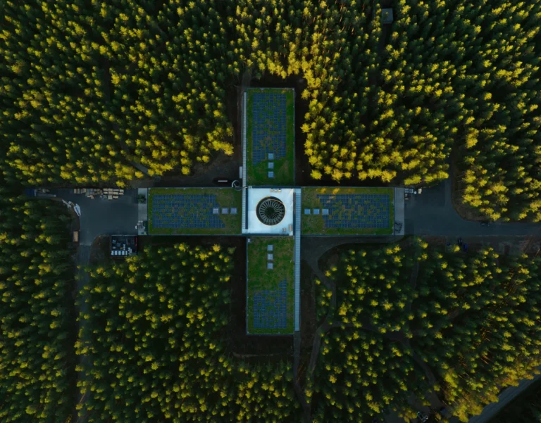 Aerial view of a cross-shaped factory building surrounded by dense pine forest in Norway.