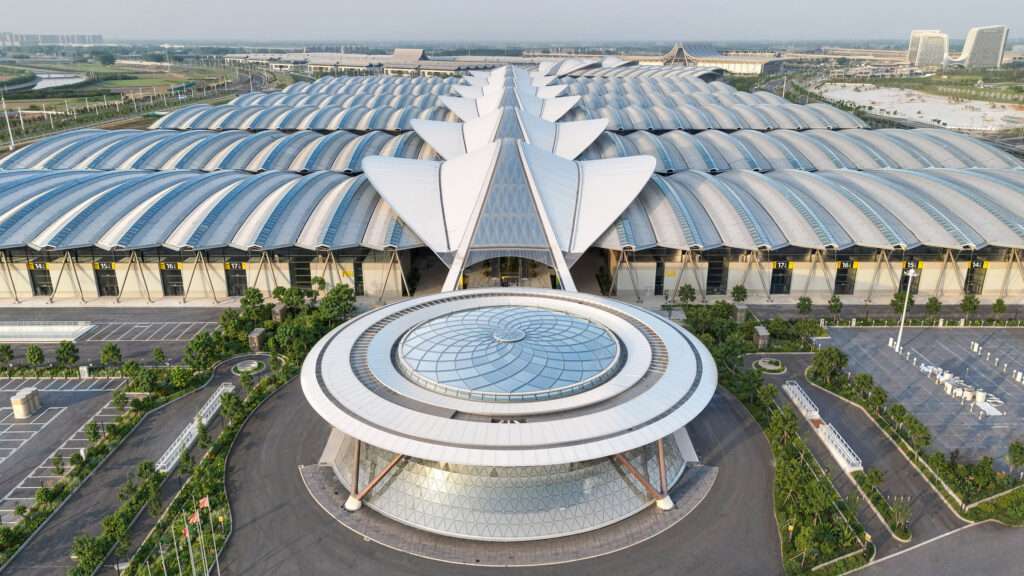 Aerial view of a massive modern convention centre with an undulating canopy roof and circular glazed entrance pavilion.