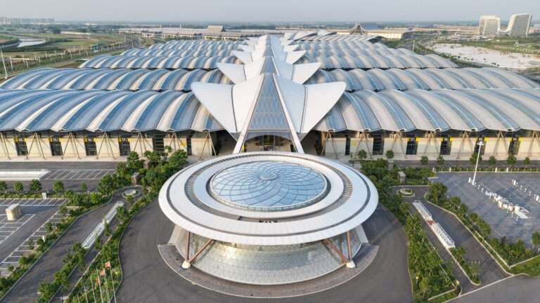 Aerial view of a massive modern convention centre with an undulating canopy roof and circular glazed entrance pavilion.