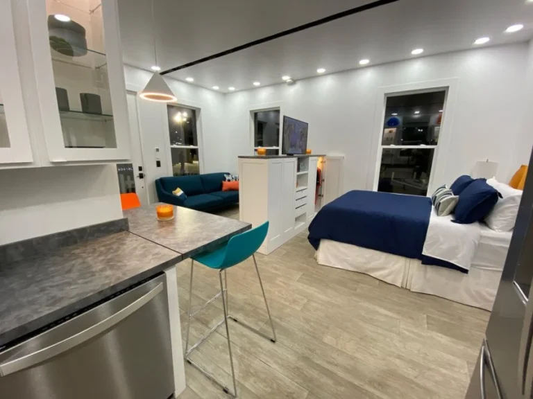Interior view of a modular housing unit showing the kitchen counter, living area, and bed.
