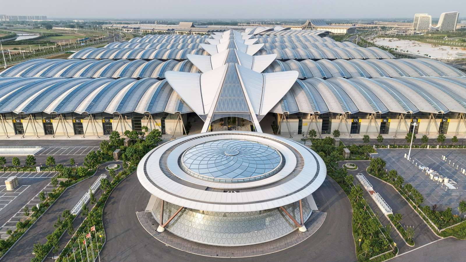 Aerial view of a massive modern convention centre with an undulating canopy roof and circular glazed entrance pavilion.