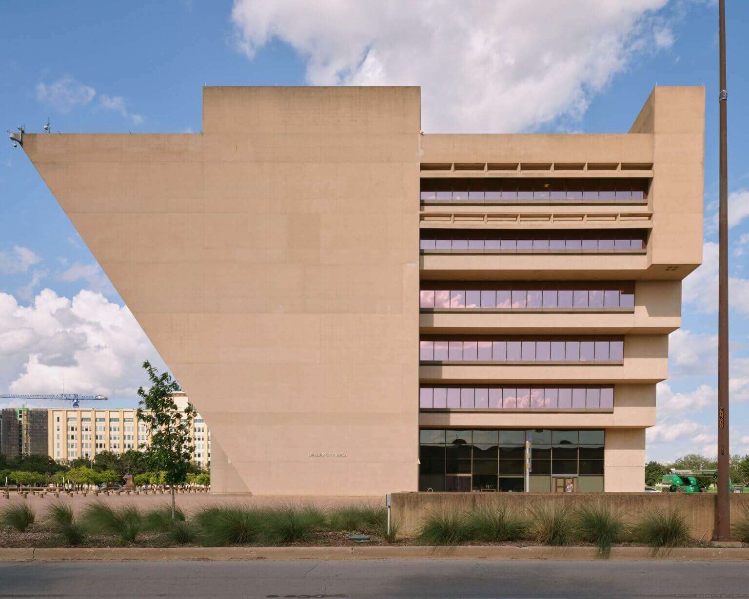 An exterior view of the Dallas City Hall showcasing its distinctive inverted Brutalist massing and cantilevered concrete facade.