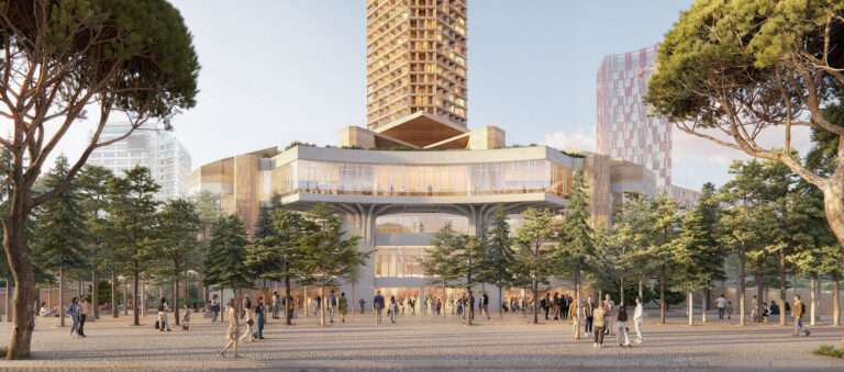 Eye-level view of a public plaza with trees leading to a glazed building entrance beneath a tower.
