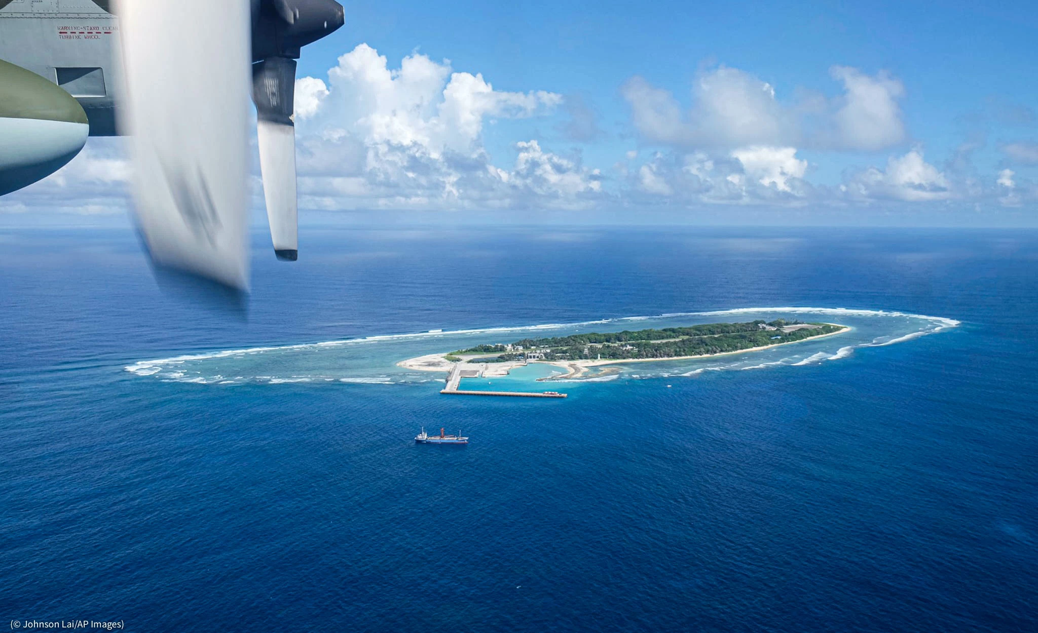 Aerial view of a thin tropical island surrounded by coral reefs and deep blue water.
