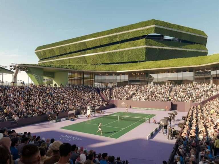 An open-air tennis stadium filled with spectators under a blue sky, featuring a green court with purple surrounds.