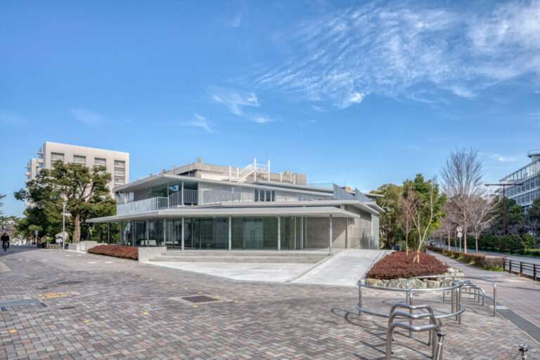 A low-rise academic building featuring glass walls and concrete overhangs along a paved pedestrian walkway.