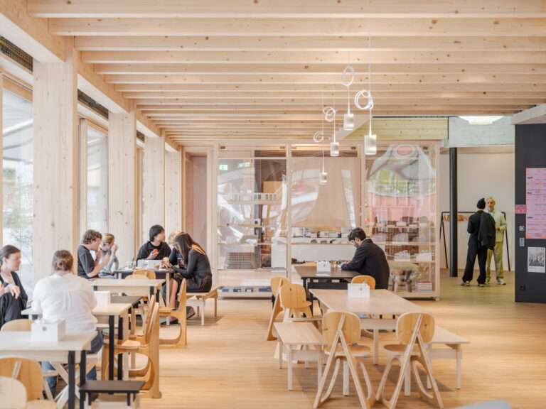 Interior view of an open-plan office cafeteria with exposed timber structural beams and wooden millwork seating.