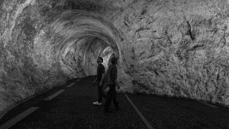 Two people walking inside a textured, rocky-patterned fabric tunnel installation with paved flooring.