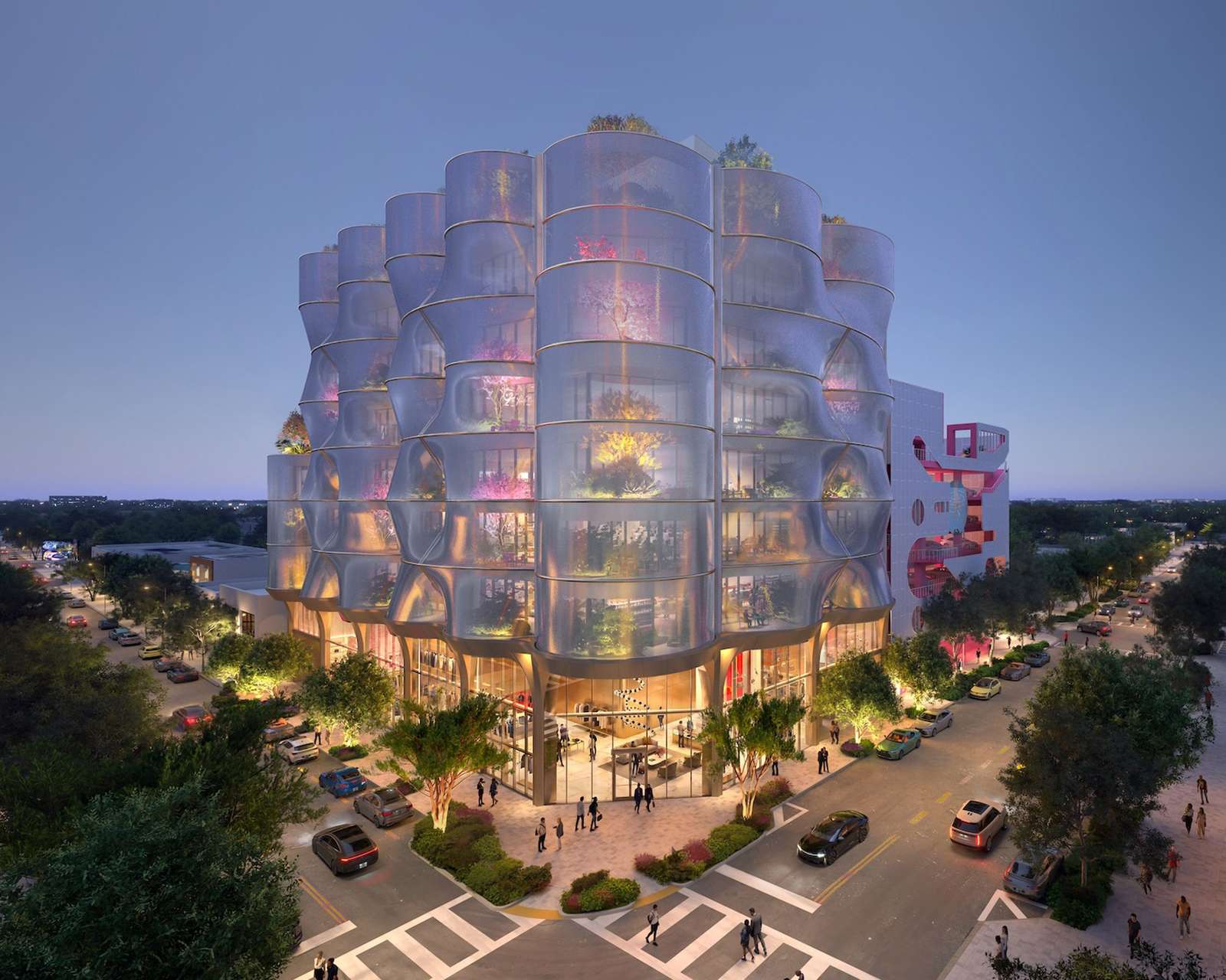 Night view of a multi-story building featuring an illuminated undulating mesh facade with internal trees visible.