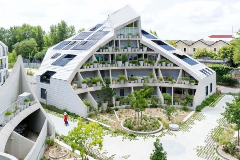 An angular residential building with light-grey tiled façades, solar panels, and numerous potted plants on tiered loggias.