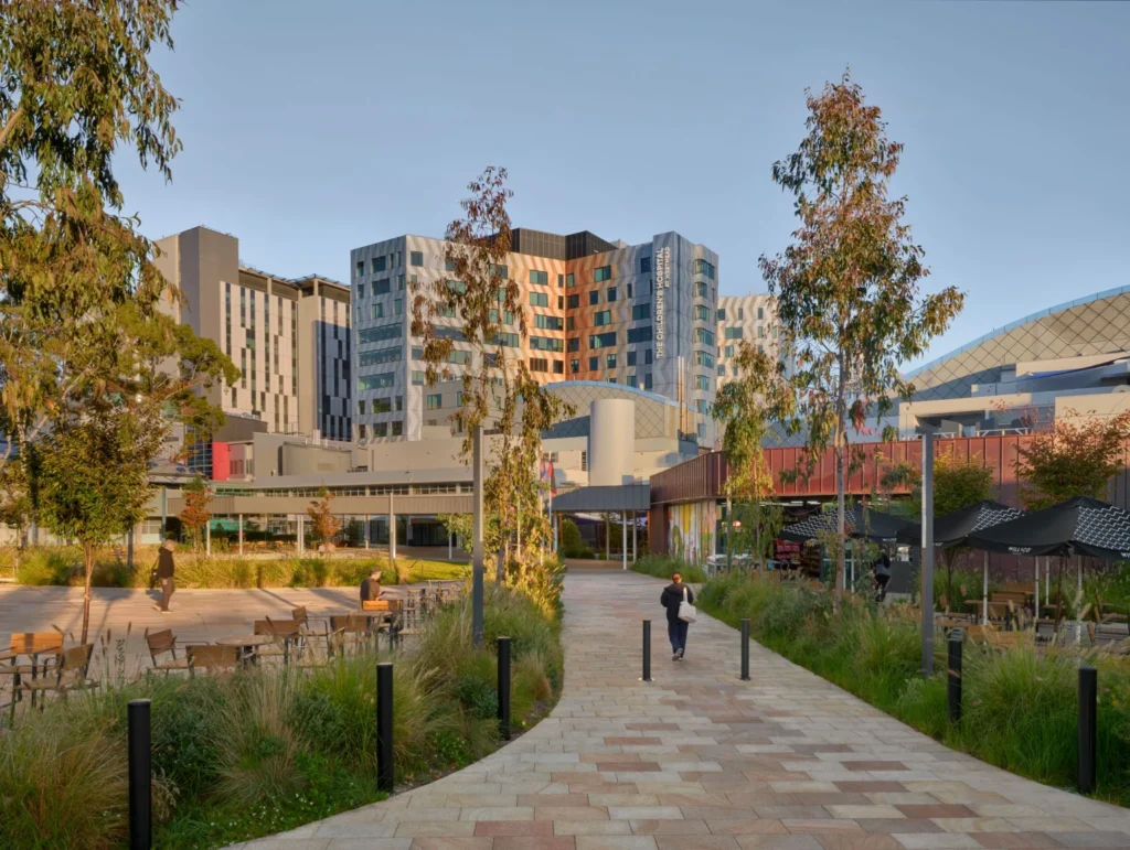 A paved pedestrian pathway winding through native landscaping toward a large modern hospital building.