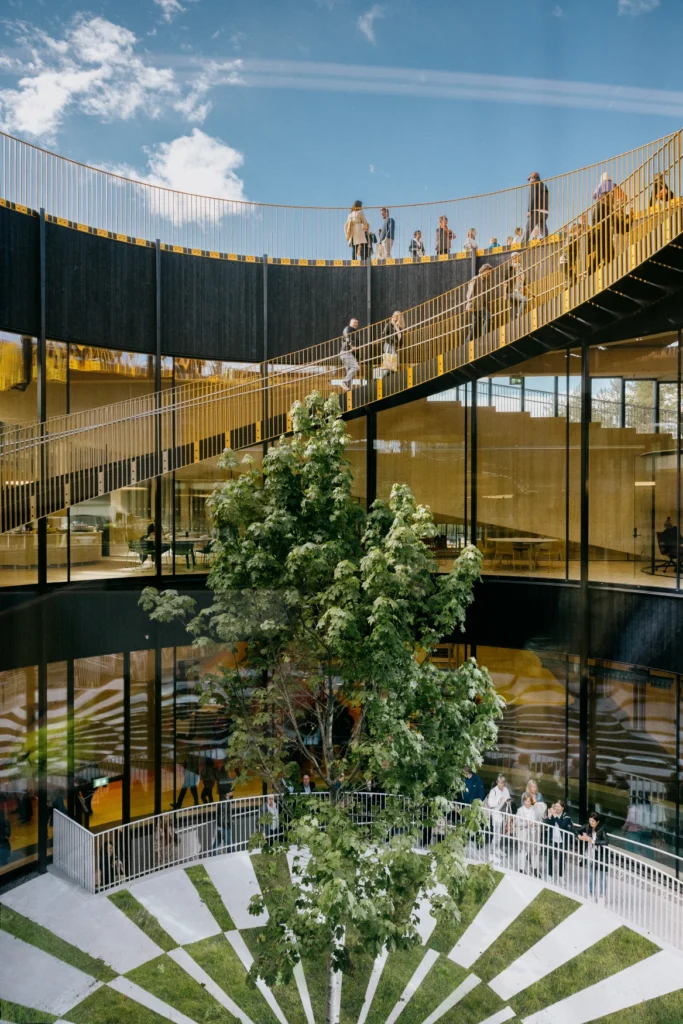 An open circular courtyard inside a timber building with an exterior spiral ramp and visitors walking.