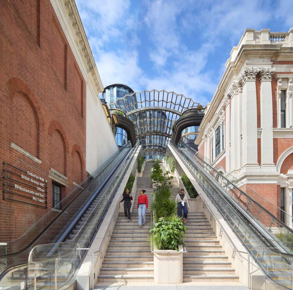 A low-angle view looking up a wide public staircase flanked by mechanical escalators and historical masonry facades.