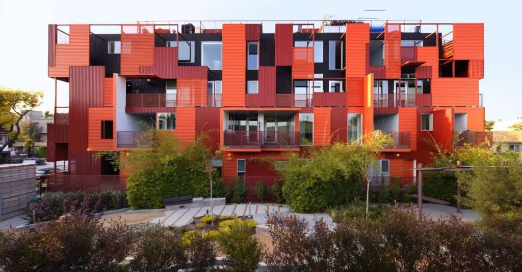 Exterior view of an apartment building with vibrant red and dark cladding modules.