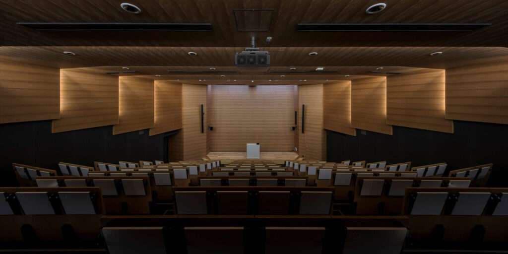 An interior viewpoint looking down toward the stage of an auditorium lined with tiered wood paneling.