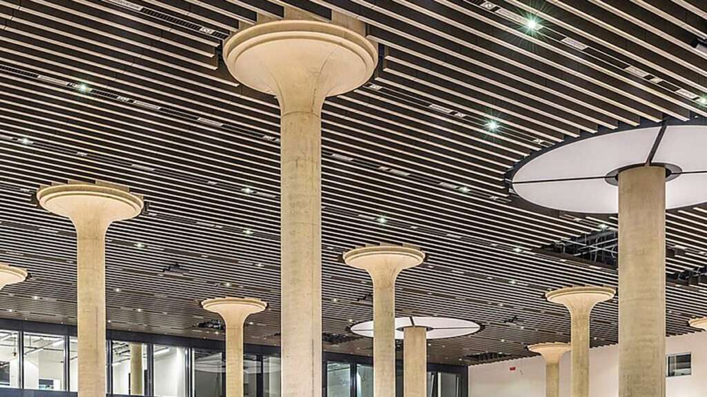 Tall concrete columns with flared tops supporting a linear slatted ceiling with integrated lighting.