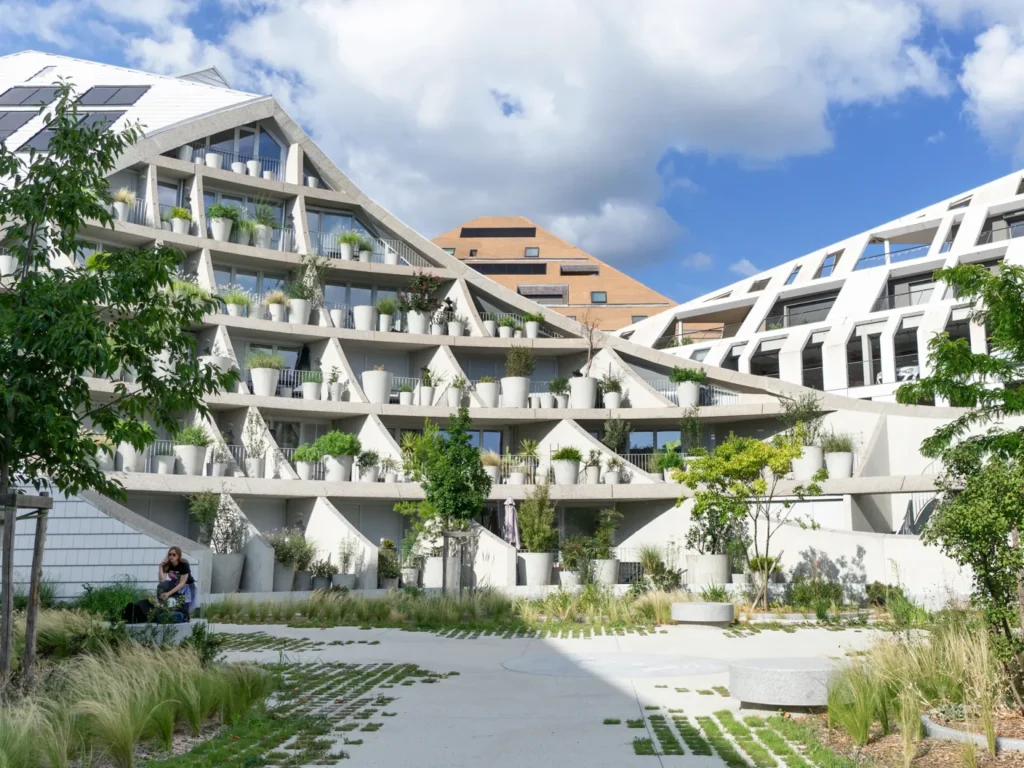 A central courtyard surrounded by stepped white apartment buildings with plant pots lining the balconies.
