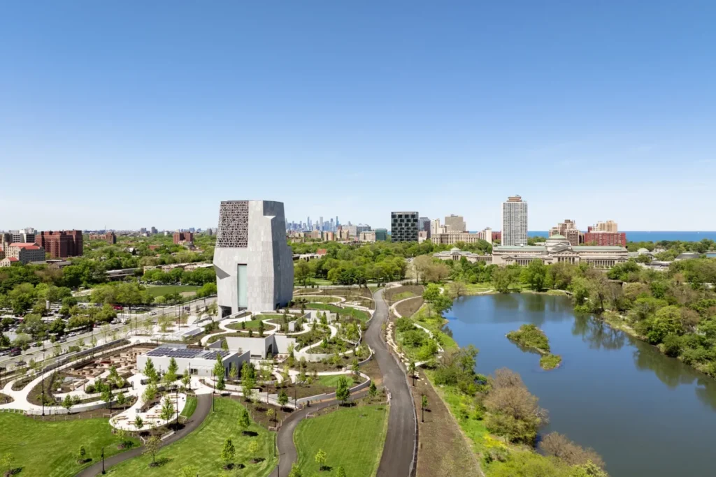 Aerial view of a modern civic campus with a stone tower next to a lagoon and parkland.