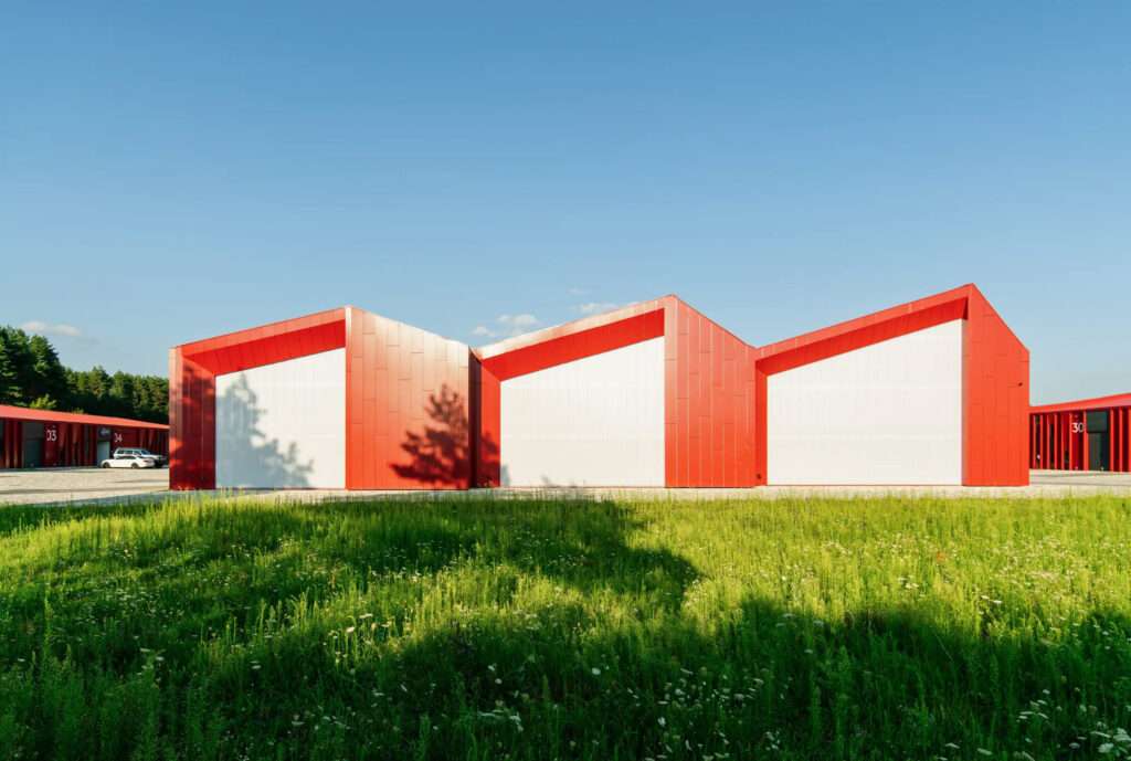 The red-framed gable ends of a building fronting a green grassy field.
