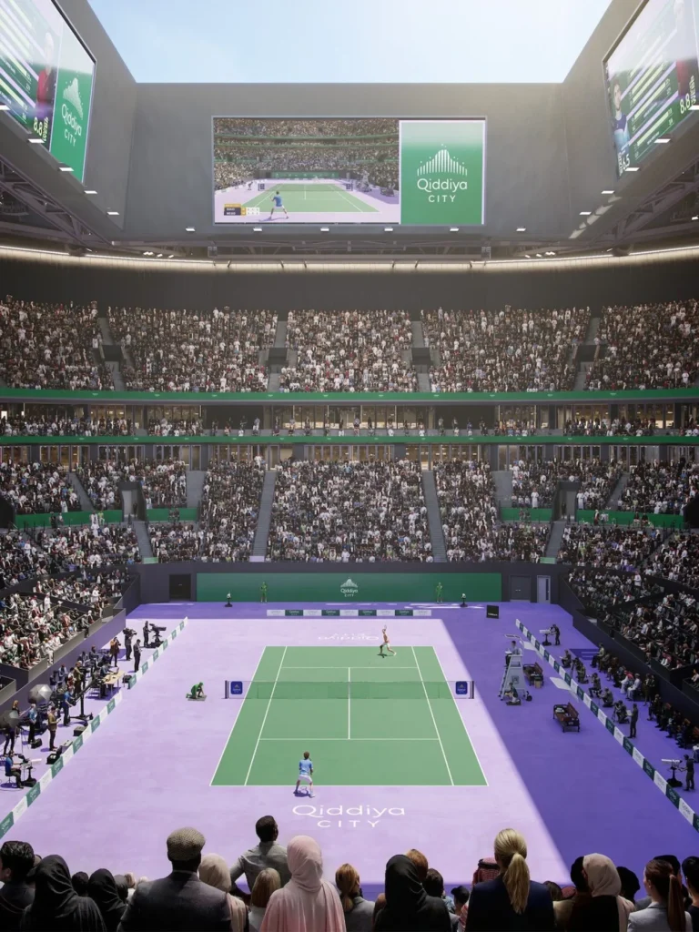 An expansive indoor tennis arena with multi-tiered spectator seating and large digital screens on upper walls.