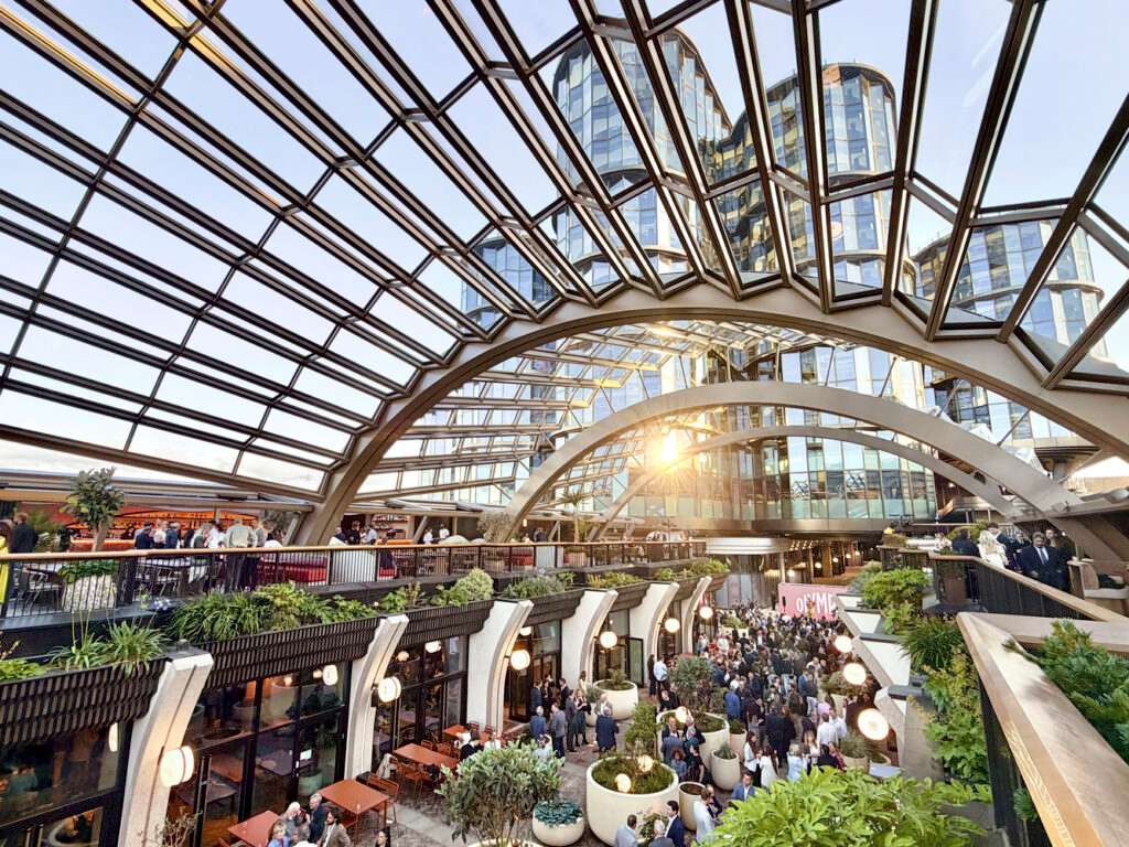 An interior perspective under a massive arched steel and glass canopy filled with a crowded public event.