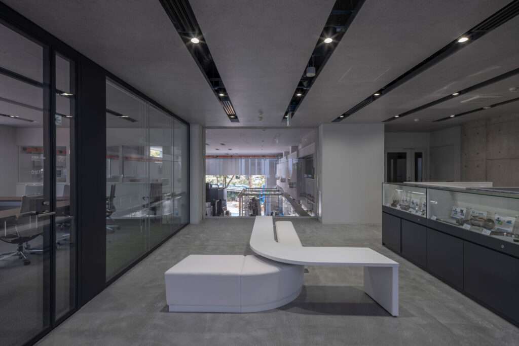 A modern concrete interior with glazed enclosures, a central sculptural white bench, and ceiling track lighting.