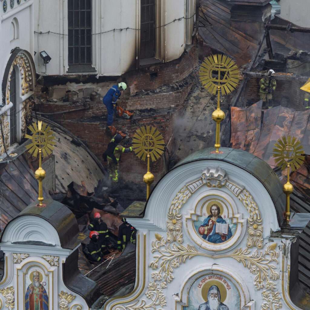 Close-up view of firefighters and emergency workers on the damaged and charred roof of the cathedral near religious iconography.