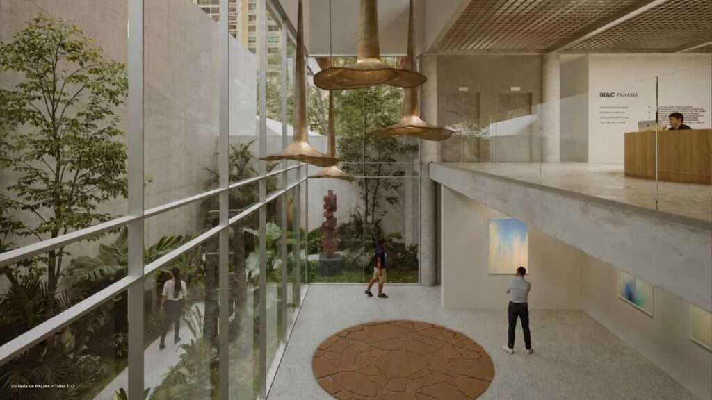 A double-height interior gallery spaces with a concrete mezzanine level, reception desk, and tall glass windows showing a courtyard.