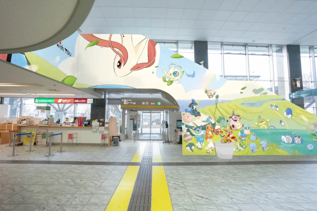 An airport arrival hall with rental car counters and a graphic wall mural leading to exits.
