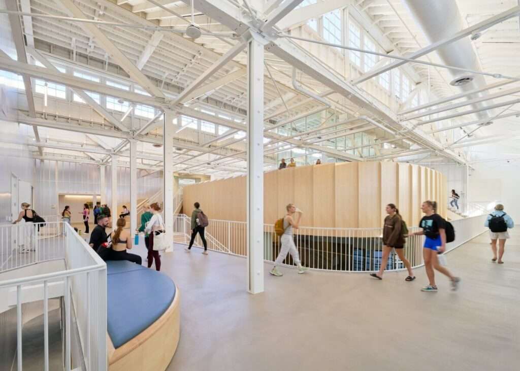 Interior view of an educational facility featuring a central curved timber millwork structure and open steel trusses.