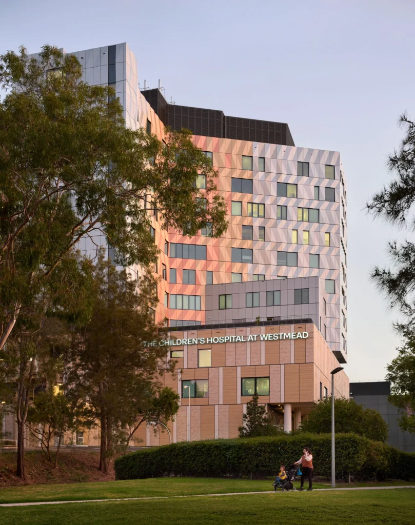 A modern hospital building showing a stone-clad podium base supporting a patterned metal panel tower.