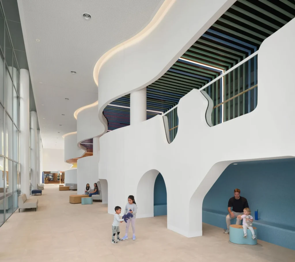 A wide white interior corridor with curvilinear architectural elements, built-in blue seating niches, and family members.
