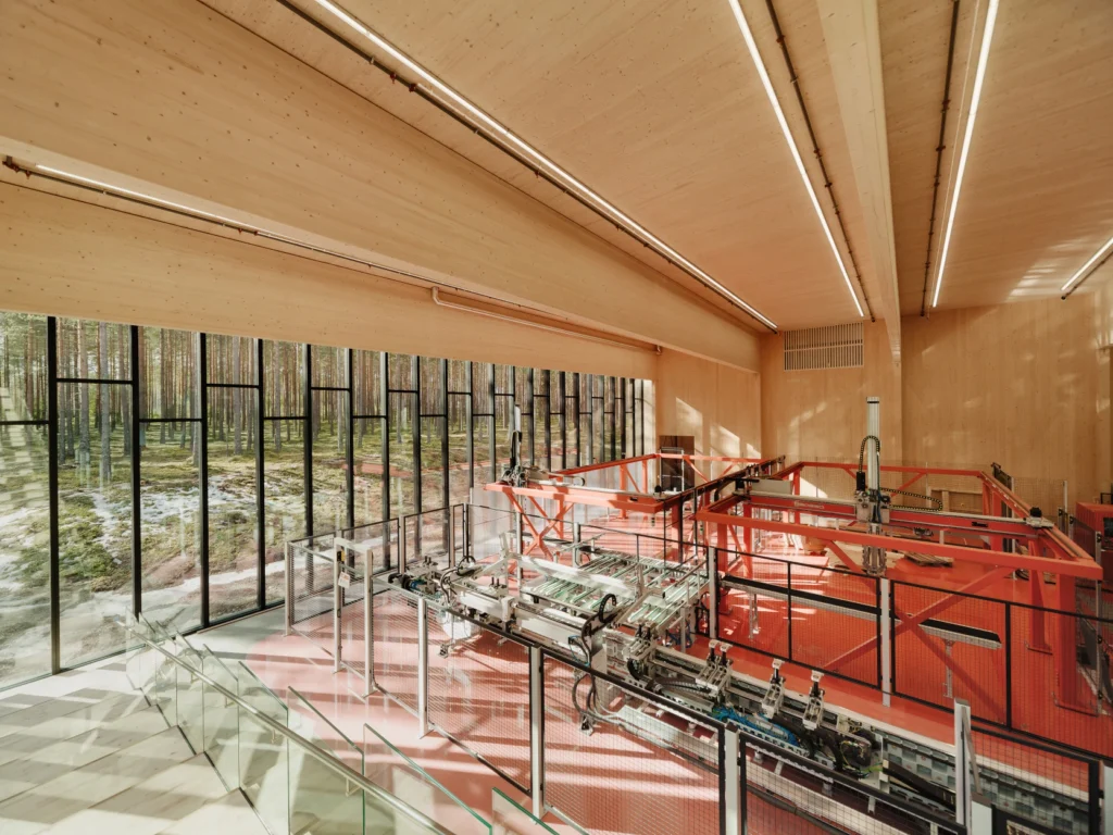 Interior view of an industrial factory hall with mass timber beams, large glass windows, and robotic machinery.