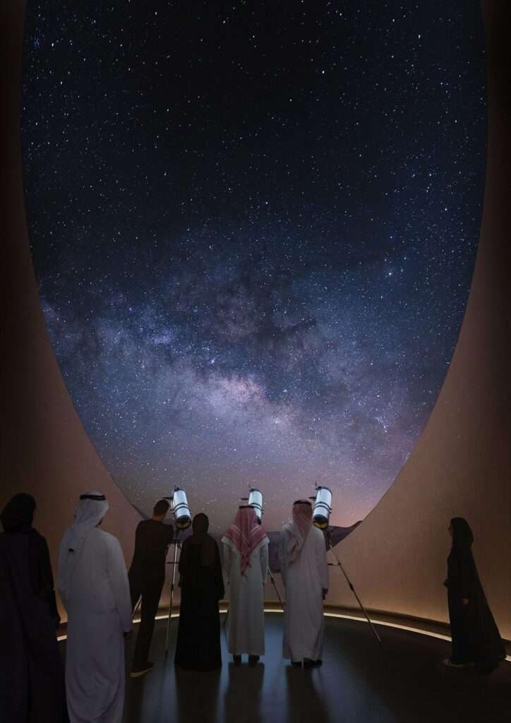 زوار داخل فتحة دائرية ينظرون عبر التلسكوبات إلى سماء الليل.