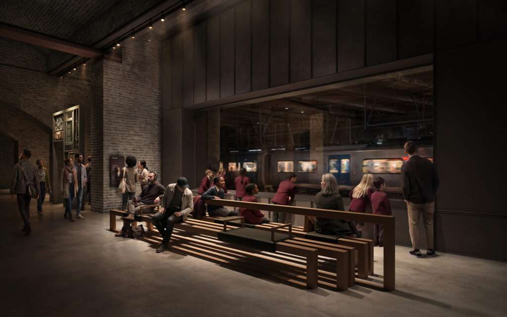 A subterranean museum gallery where visitors look through a large glass window at an active transit train line.
