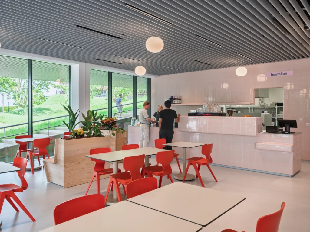 A modern museum café interior featuring a pink tiled service counter and bright red chairs.