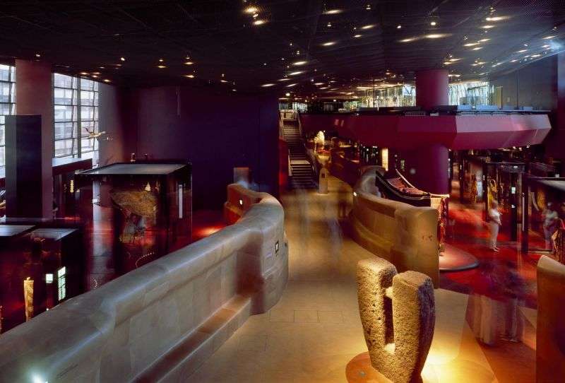 Wide interior view of a fluid, dimly lit museum hall with curved low walls and built-in display vitrines.