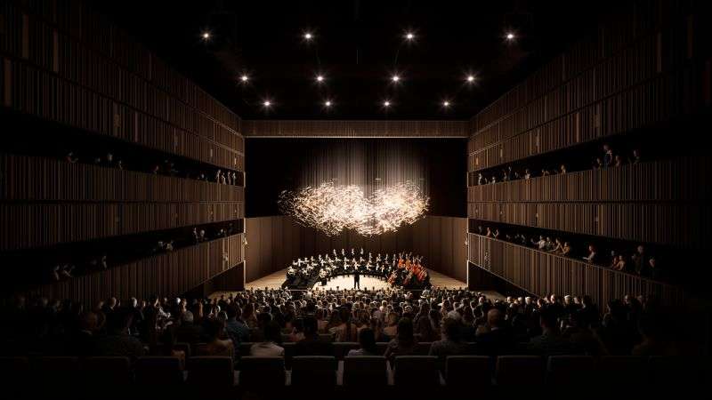 An auditorium filled with an audience watching a live orchestra perform on stage under a light installation.