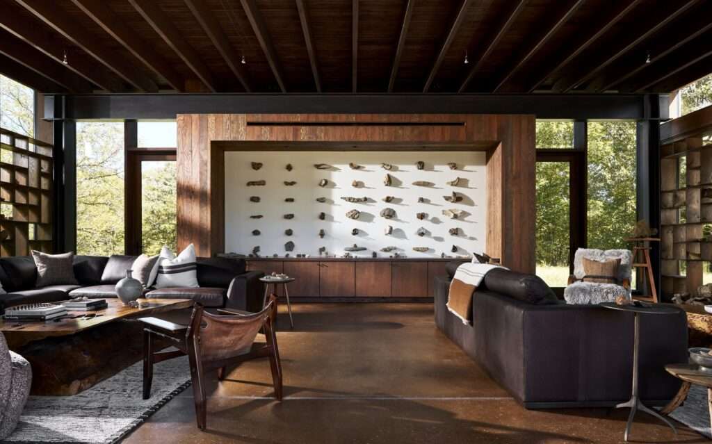 Spacious interior of the Rock Pavilion with dark leather couches, polished concrete floors, steel columns, and a large central white wall showcasing a grid of mounted geological rock specimens.