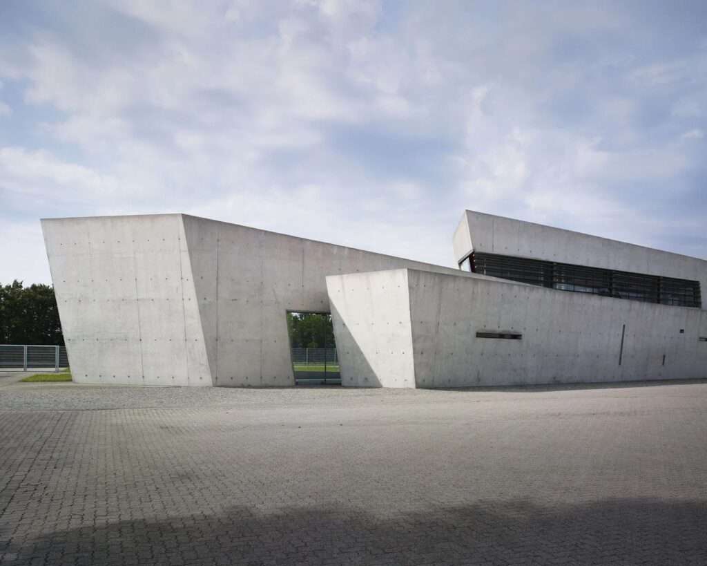 Overlapping cast-in-place concrete walls of the Vitra Fire Station under a cloudy sky.