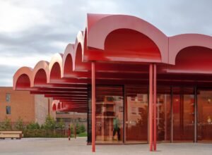 Architectural detail of the deep red vaulted roof structure of the O-day'min Park Pavilion in Edmonton, highlighting its rhythmic curves and steel construction.