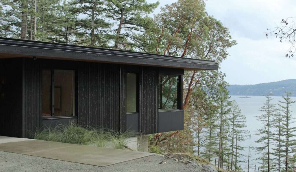 Hilltop House modern coastal residence featuring dark vertical wood cladding and large glass windows overlooking Salish Sea.