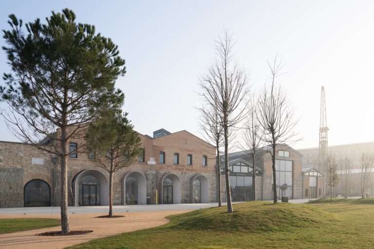 Exterior view of the brick facade of Beymen Tersane with historical arched entryways and a landscaped green plaza under a clear sky.