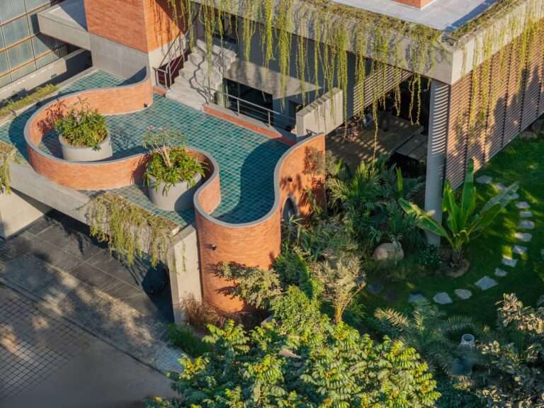 Aerial view of Valaya House showing a curved red brick wall feature, green tiled terrace, and lush tropical landscaping in Ahmedabad.