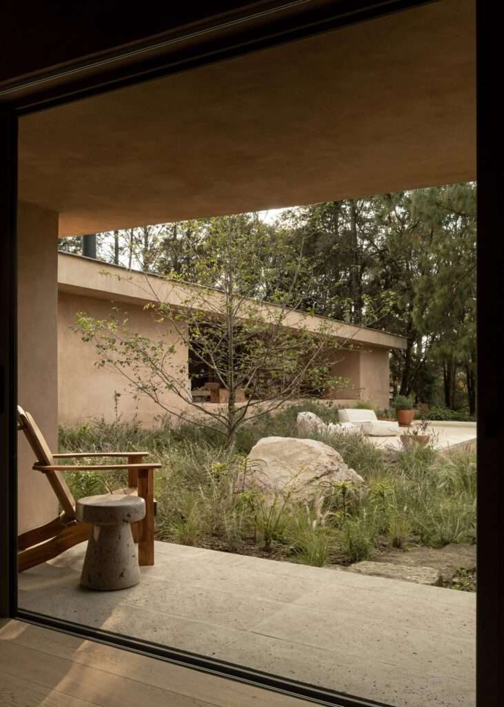 Full front view of a long, single-story monochromatic pavilion with large glass windows built on a terraced slope next to a pond.